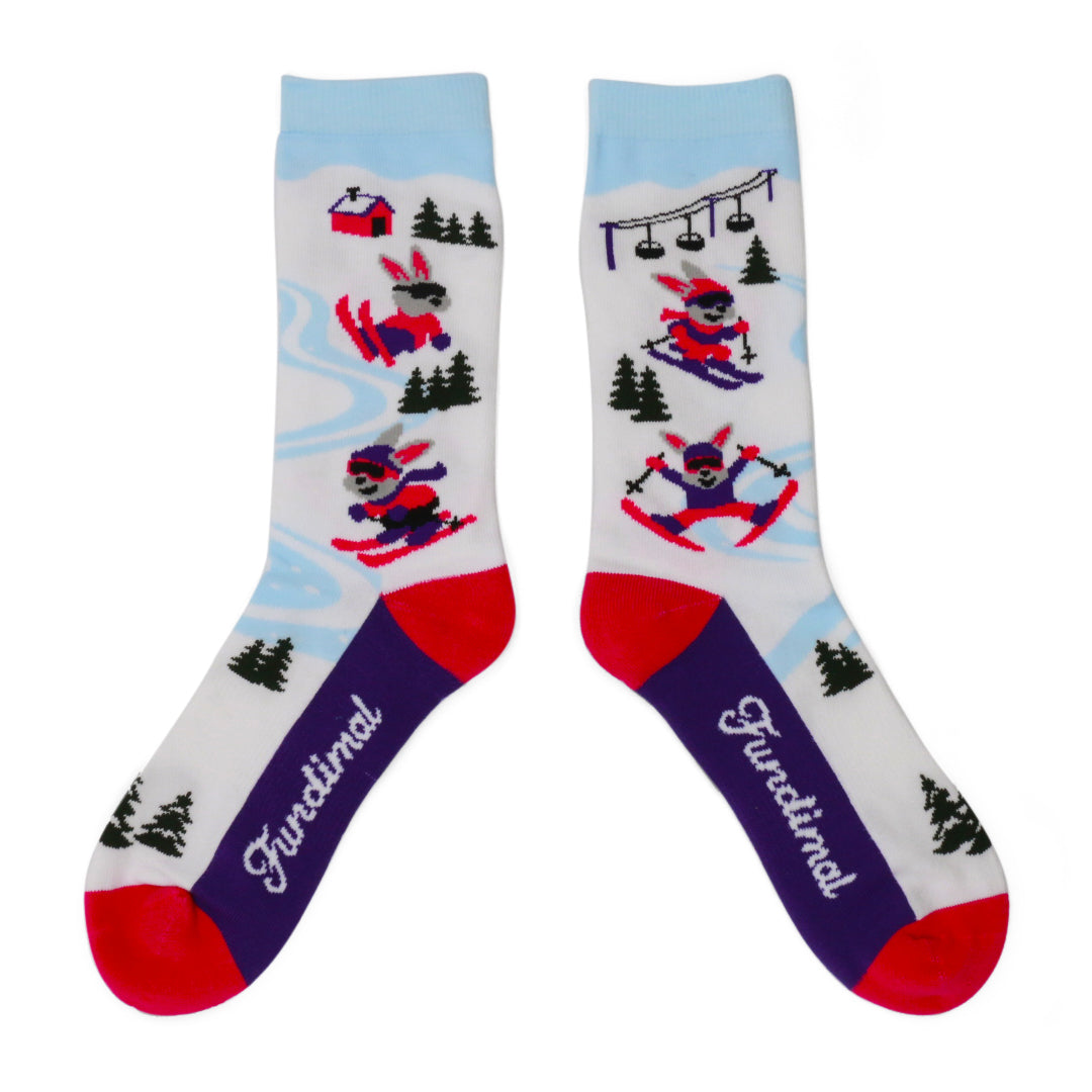 Pair of Adult Ski Bunny Socks with skiing rabbits and evergreen trees on pale blue legs, with purple feet and red heels and toes.